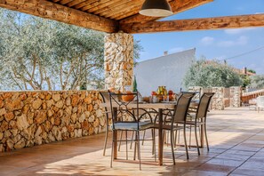 An outdoor patio with stone walls, wooden beams, and a table set for dining. - Mas Gauda – Garden & family space, Côte d’Azur (La Gaude)