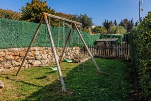 Un columpio de madera en un patio trasero con un muro de piedra y una valla de madera.