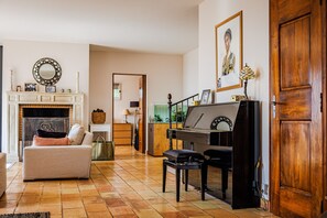A living room with a fireplace, a piano, a sofa, and a dining area.