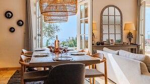 Un comedor con una mesa de madera dispuesta para cuatro personas, una lámpara colgante de mimbre y vistas al exterior.