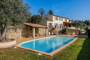 Una piscina con plataforma de piedra, pared de piedra y un árbol grande.