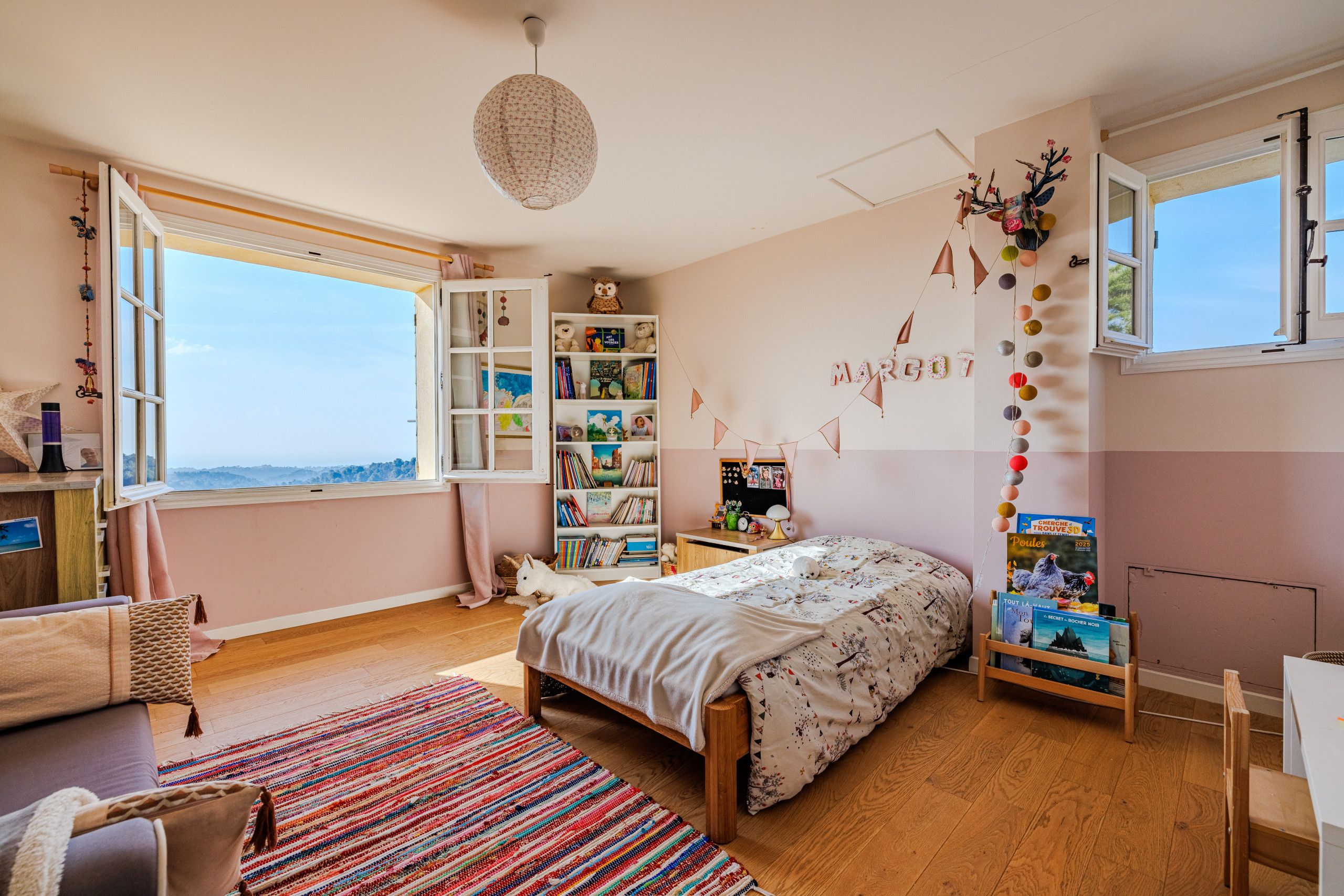 Um quarto com uma janela grande, uma cama, uma estante e uma mesa.