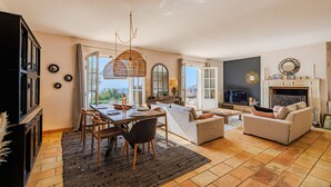 Amplia sala de estar con comedor, chimenea y ventanas grandes que ofrecen vistas al exterior.