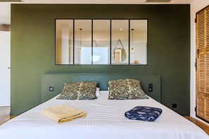 A bed with a checkered bedspread, two floral pillows, and a folded blanket on a green wall. - Mas Gauda – Garden & family space, Côte d’Azur (La Gaude)