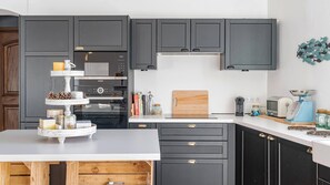 A modern kitchen with dark cabinetry, a central island, and a variety of appliances including a stove, oven, and microwave.