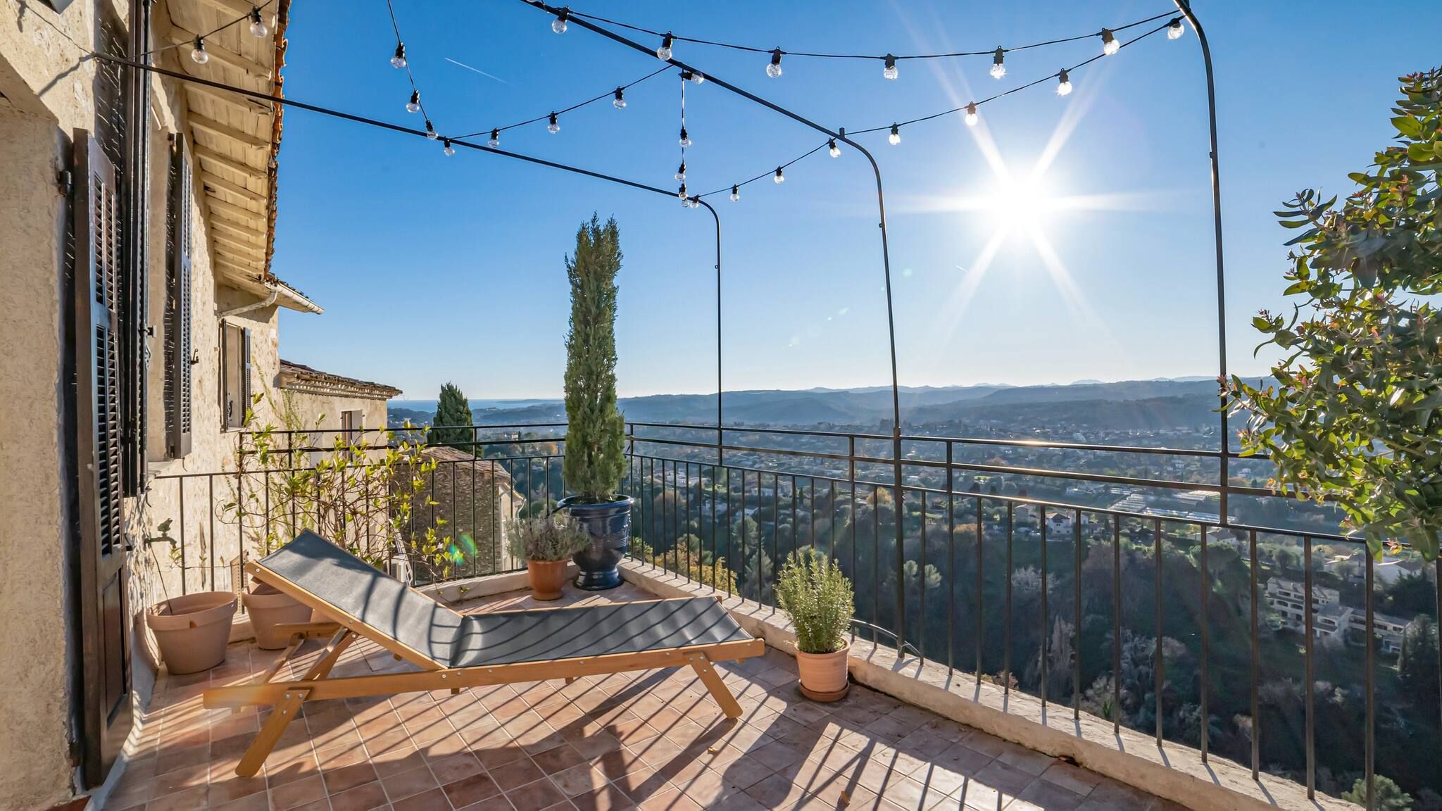 Ein Balkon mit Liegestuhl, Topfpflanzen und Lichterkette.