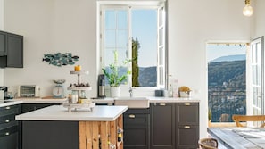 A modern kitchen with dark cabinets, a white island, and a large window offering a view of the countryside.