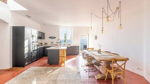 A modern kitchen with a central island, dark cabinets, and a dining area with a wooden table and chairs. - Apt Chagall – In the heart of Saint-Paul de Vence (Saint Paul de Vence)