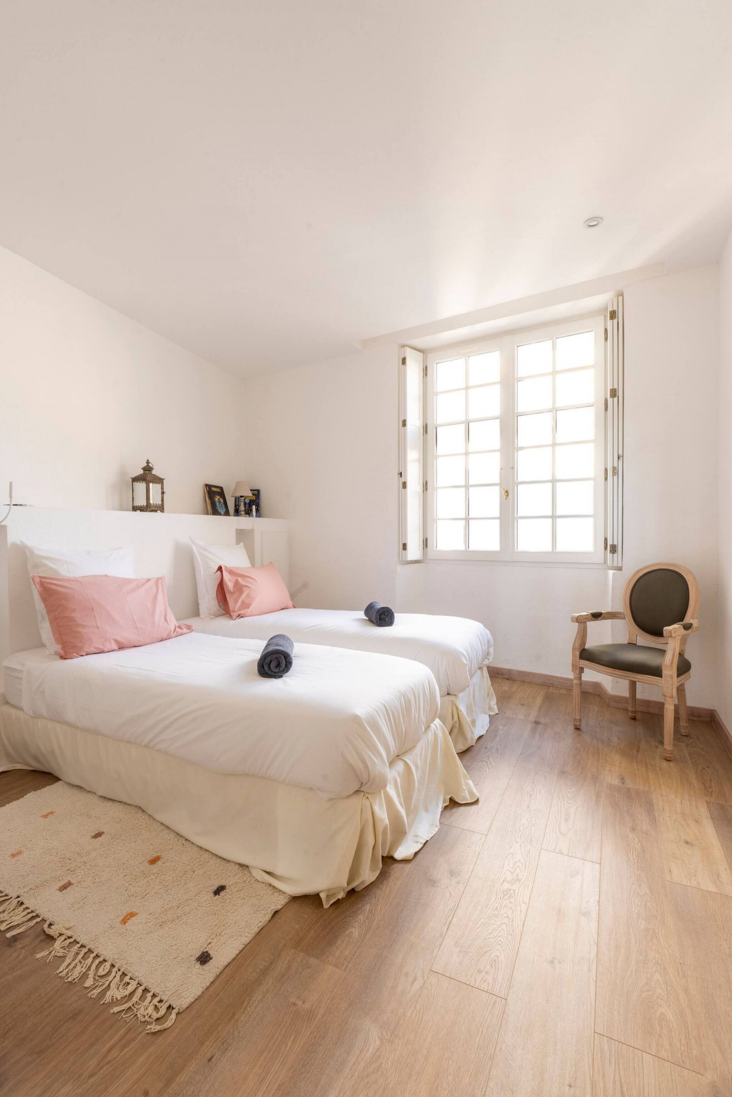 A bedroom with two beds, a wooden floor, a window, and a chair.