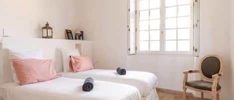 A bedroom with two beds, a wooden floor, a window, and a chair.