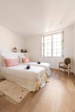 A bedroom with two beds, a wooden floor, a window, and a chair. - Apt Chagall – In the heart of Saint-Paul de Vence (Saint Paul de Vence)