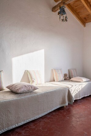 A cozy bedroom with two beds, striped pillows, a teddy bear, and a wooden ceiling beam.
