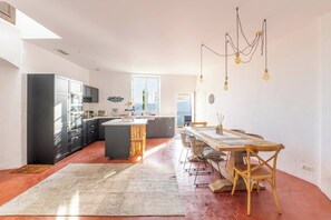 A modern kitchen with a central island, dark cabinets, and a dining area with a wooden table and chairs. - Apt Chagall – In the heart of Saint-Paul de Vence (Saint Paul de Vence)
