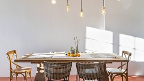 A dining area with a wooden table, wicker chairs, and hanging pendant lights.