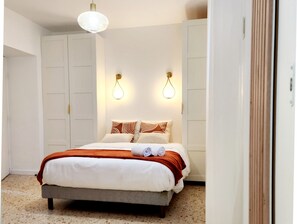 A neatly made bed with a white and brown bedspread, two wall-mounted light fixtures, and a large wardrobe. - Le 56 entre ville&lac sejouraixlesbains (Aix-les-Bains)