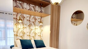 A bedroom with a bed, a wooden headboard, a wall-mounted mirror, and a ceiling light fixture. - Le 56 entre ville&lac sejouraixlesbains (Aix-les-Bains)