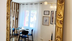 A dining area with a table, chairs, and a view through a large mirror with ornate gold framing. - Le 56 entre ville&lac sejouraixlesbains (Aix-les-Bains)