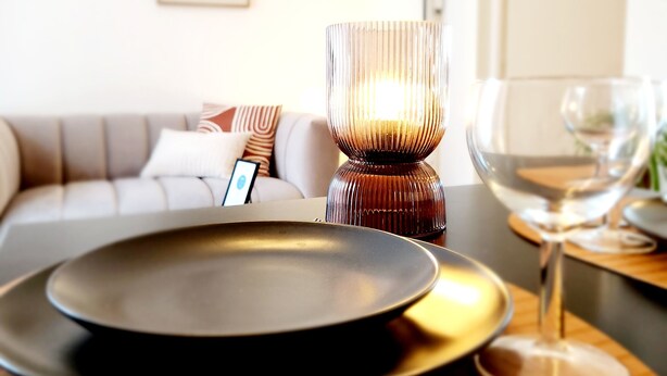A modern dining area with a candle holder, a glass, and a plate on a table. - Le 56 entre ville&lac sejouraixlesbains (Aix-les-Bains)