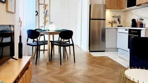 A modern kitchen with wooden cabinets, a stainless steel refrigerator, and a dining area with a wooden table and black chairs. - Le 56 entre ville&lac sejouraixlesbains (Aix-les-Bains)