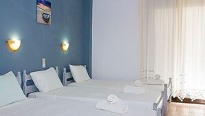 A hotel room with two beds, white linens, and a view of the sea through sheer curtains. - La Pensione Skiathos (Skiathos)