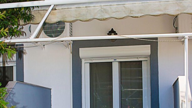 A small patio with a table and two chairs, a sliding glass door, and a white awning. - La Pensione Skiathos (Skiathos)