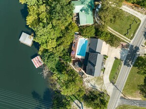 An aerial view of a lakeside property with a swimming pool, a dock, and a road nearby. - Lake Shore Landing For 20! (Branson)