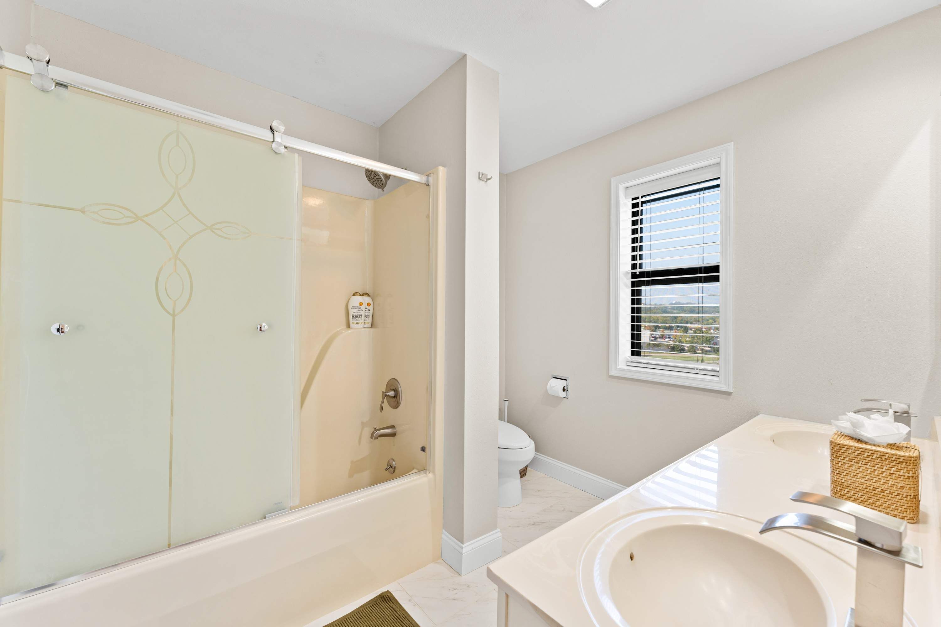 Un baño moderno con ducha envuelta en vidrio, inodoro y lavamanos con una cesta de mimbre.