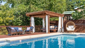 En swimmingpool med træterrasse, liggestole og pergola.