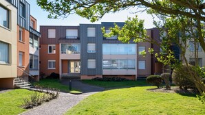 A modern multi-story residential building with balconies, a well-maintained lawn, and a gravel pathway.