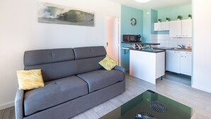 A modern living room with a grey sofa, a coffee table, and a kitchen area with white cabinets and a microwave.