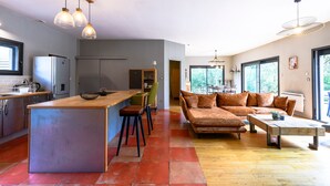 A modern kitchen with a central island, a dining area with a sofa and coffee table, and large windows offering natural light. - Chemin de Ronze - Maison au calme avec piscine (Labastide-de-Virac)