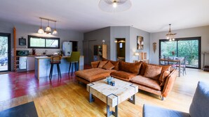 A modern living room with a sectional sofa, a coffee table, and a dining area with a table and chairs. - Chemin de Ronze - Maison au calme avec piscine (Labastide-de-Virac)