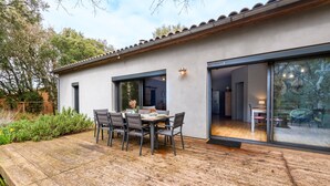 A modern house with a patio, a dining table with chairs, and a large sliding glass door leading to an interior space. - Chemin de Ronze - Maison au calme avec piscine (Labastide-de-Virac)