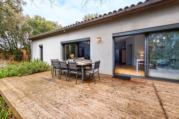 A modern house with a patio, a dining table with chairs, and a large sliding glass door leading to an interior space.