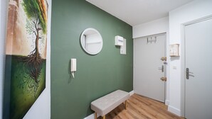 Un pasillo con pared verde, un espejo redondo, un banco y una puerta con pomo.