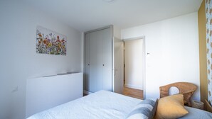 Un dormitorio con una cama, una puerta, una silla y un cuadro en la pared.
