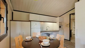 Une cuisine compacte avec des meubles blancs, un four à micro-ondes et un évier. On y trouve une table à manger avec quatre chaises et un panier.