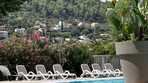 Un espace piscine doté de chaises longues et offrant une vue sur une colline parsemée de maisons.
