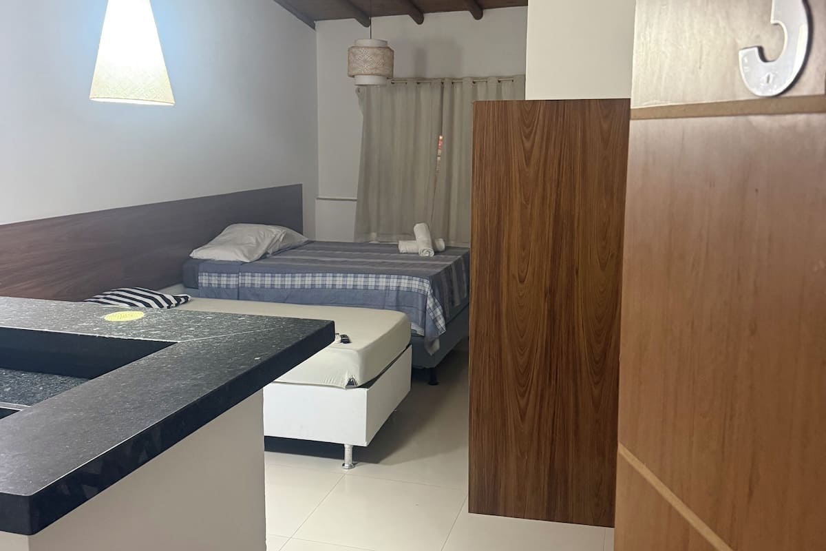 Een hotelkamer met een houten plafond, een bed met een blauw-wit geruit sprei, een witte nachtkastje en een aan de muur bevestigd nummer '3'.