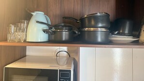 Un estante de cocina con varias ollas, una tetera y vasos.
