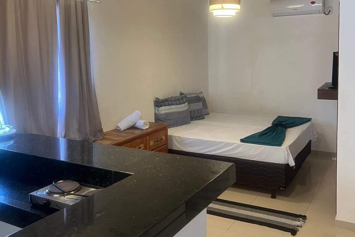 Een compacte hotelkamer met een bed, nachtkastje en een klein keukentje.