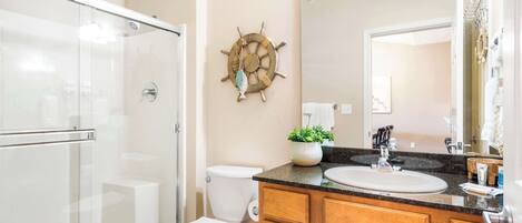 Un baño con cabina de ducha de vidrio, inodoro, lavabo con tocador y un barco decorativo en la pared.