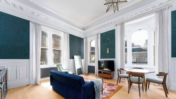 Amplia sala de estar con sofá azul, mesa de comedor de madera y sillas, ventanas grandes con cortinas y una chimenea.