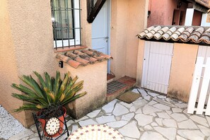 A stone patio with a potted plant, a tiled roof, and a white gate.