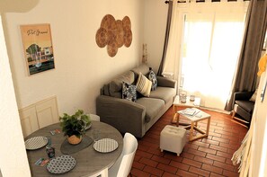 A living room with a sofa, a dining table with plates, a plant, and a wall art piece.