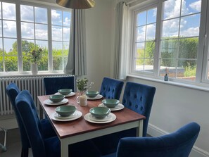 Zona pranzo con tavolo apparecchiato per quattro, sedie imbottite blu, piatti bianchi e ciotole verdi.