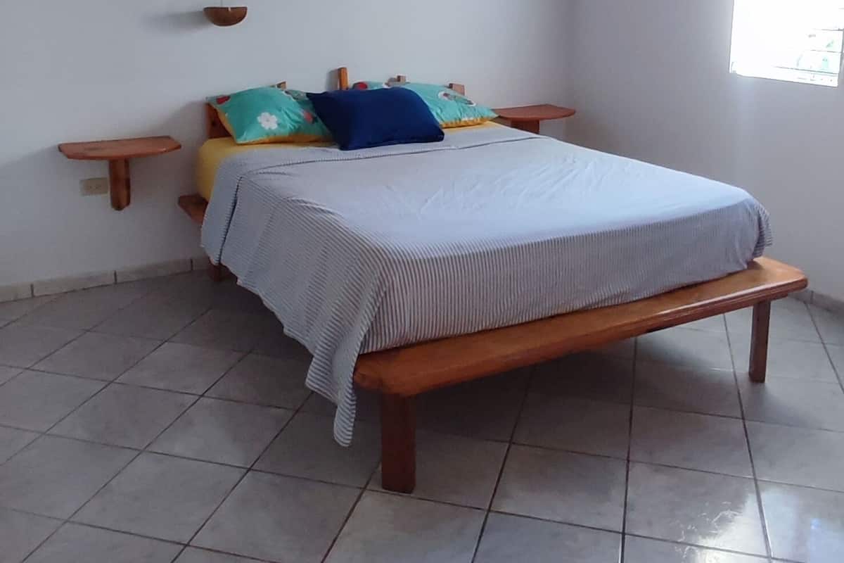 A bedroom with a wooden bed, a ceiling fan, a window, and a tiled floor.