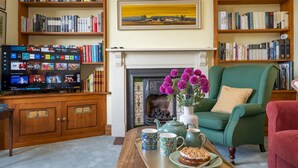 A cozy living room with a fireplace, bookshelves, a television, and a dining table with a cake. - Quintessentially English 3-Bed Home in Ludlow - Pass the Keys (Ludlow)