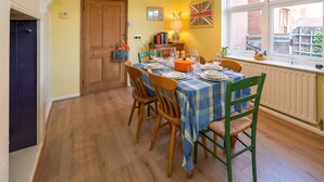 A dining area with a table set for four, wooden chairs, a blue tablecloth, and a window with a view of a brick building. - Quintessentially English 3-Bed Home in Ludlow - Pass the Keys (Ludlow)