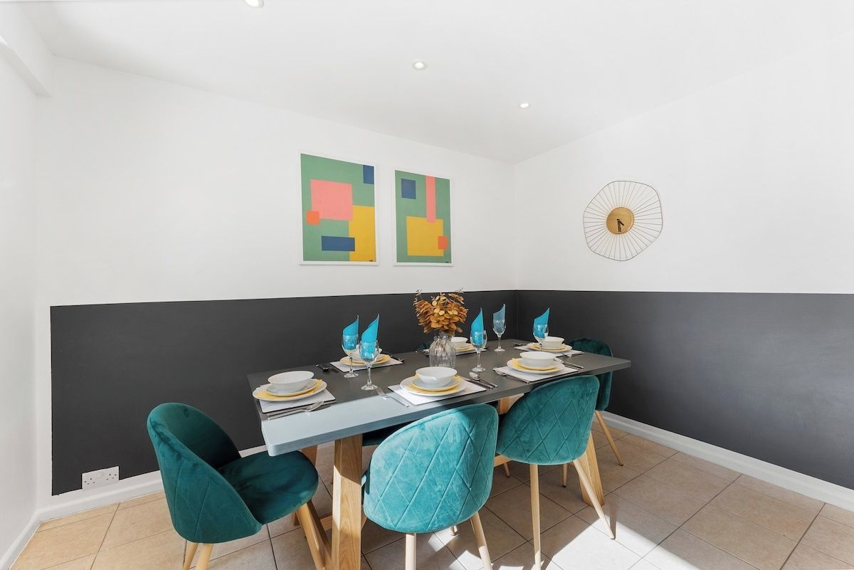 A dining area with a table set for four, teal chairs, and abstract wall art.